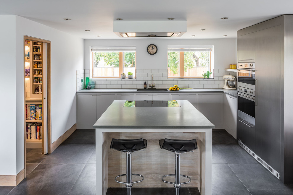 Design ideas for a mid-sized contemporary l-shaped kitchen in Berkshire with a single-bowl sink, flat-panel cabinets, white cabinets, white splashback, subway tile splashback, stainless steel appliances, with island, grey floor and grey benchtop.