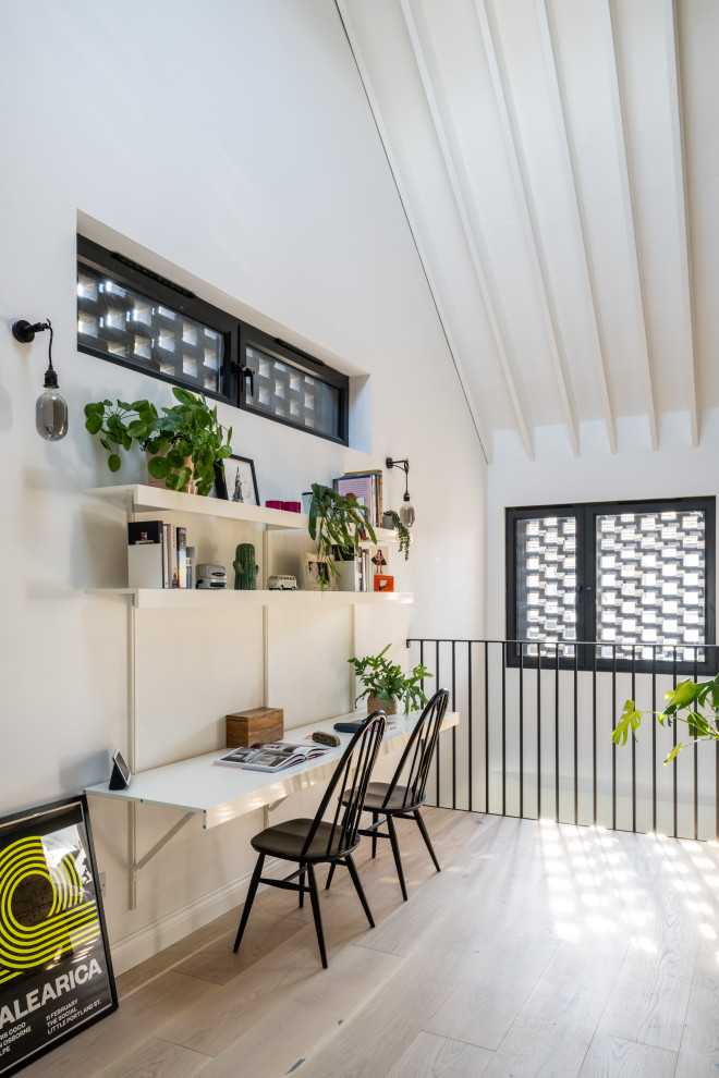 Modernes Arbeitszimmer mit weißer Wandfarbe, hellem Holzboden, Einbau-Schreibtisch, beigem Boden, freigelegten Dachbalken und gewölbter Decke in London