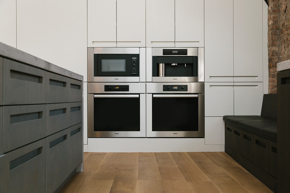 Photo of an industrial kitchen in New York with light hardwood floors and with island.