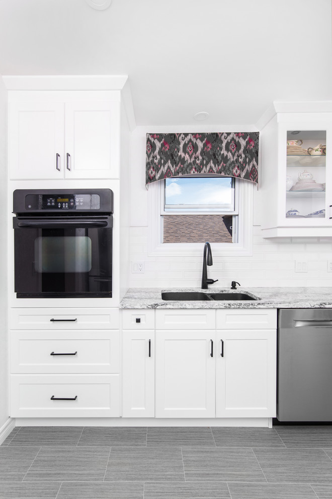 Example of a mid-sized transitional galley porcelain tile and gray floor eat-in kitchen design with a double-bowl sink, shaker cabinets, white cabinets, granite countertops, white backsplash, subway tile backsplash, stainless steel appliances, no island and gray countertops