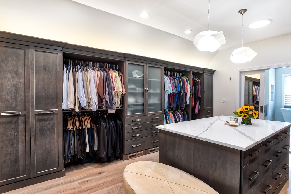 Design ideas for an expansive transitional gender-neutral walk-in wardrobe in New York with flat-panel cabinets, dark wood cabinets and light hardwood floors.