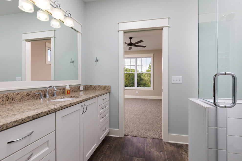 Inspiration for a mid-sized traditional bathroom in Grand Rapids with recessed-panel cabinets, white cabinets, an alcove shower, a one-piece toilet, white tile, subway tile, an undermount sink, granite benchtops, brown floor, a hinged shower door and beige benchtops.