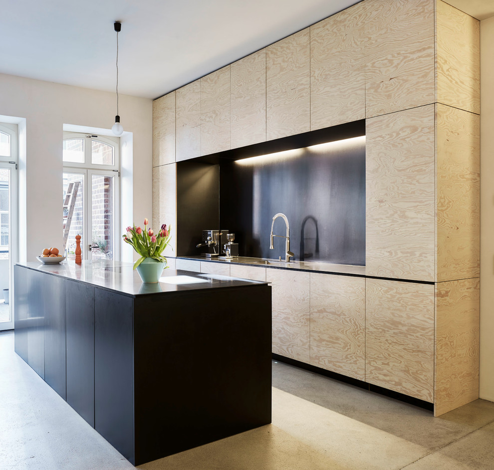 This is an example of a mid-sized industrial galley open plan kitchen in Leipzig with a drop-in sink, flat-panel cabinets, medium wood cabinets, black splashback, concrete floors, multiple islands and grey floor.