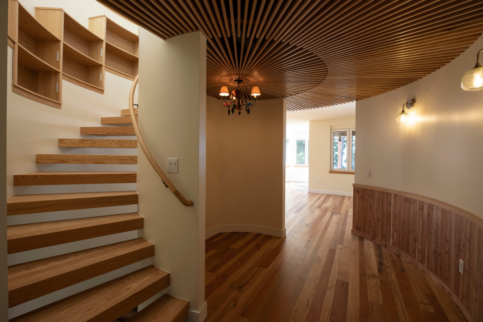 На фото: изогнутая лестница в современном стиле с деревянными ступенями, деревянными перилами и панелями на стенах без подступенок