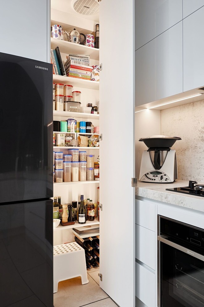 This is an example of a mid-sized contemporary u-shaped kitchen in Melbourne with an undermount sink, white cabinets, solid surface benchtops, beige splashback, porcelain splashback, black appliances, ceramic floors and beige benchtop.