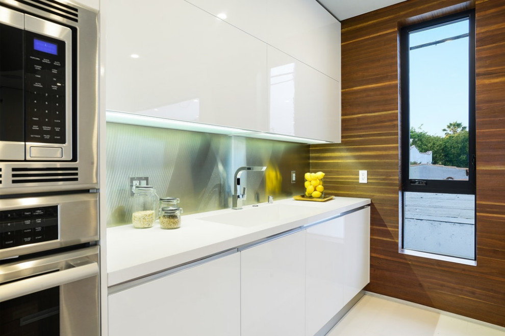 This is an example of a mid-sized modern u-shaped open plan kitchen in Los Angeles with flat-panel cabinets, white cabinets, quartzite benchtops, metallic splashback, metal splashback, stainless steel appliances, with island, white floor and white benchtop.