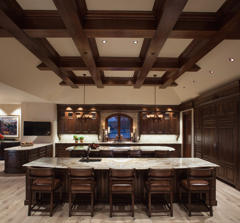 This is an example of an expansive country u-shaped open plan kitchen in Calgary with an undermount sink, recessed-panel cabinets, dark wood cabinets, granite benchtops, grey splashback, stone tile splashback, panelled appliances, light hardwood floors and multiple islands.