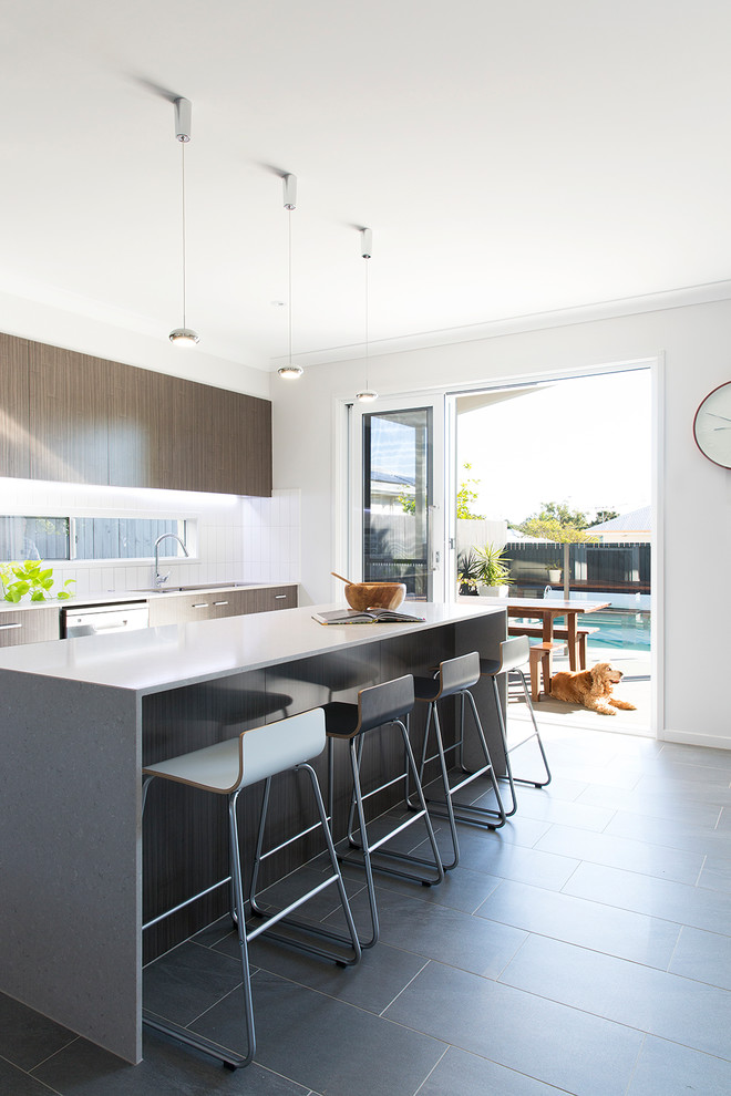 Contemporary galley open plan kitchen in Brisbane with an undermount sink, recessed-panel cabinets, medium wood cabinets, solid surface benchtops, white splashback, subway tile splashback, stainless steel appliances, ceramic floors, with island and grey floor.