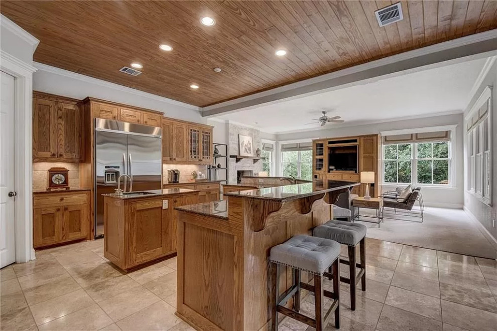 This is an example of a large beach style l-shaped open plan kitchen in Austin with an undermount sink, raised-panel cabinets, medium wood cabinets, granite benchtops, beige splashback, stone tile splashback, stainless steel appliances, travertine floors, multiple islands, white floor, brown benchtop and wood.