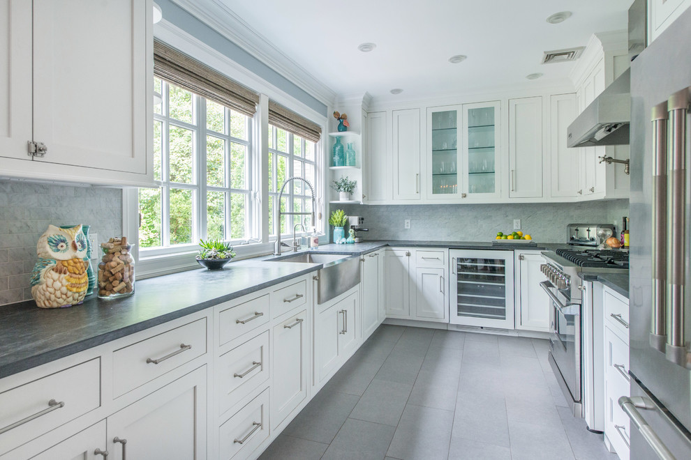 Enclosed kitchen - mid-sized transitional u-shaped gray floor and porcelain tile enclosed kitchen idea in New York with a farmhouse sink, recessed-panel cabinets, white cabinets, gray backsplash, marble backsplash, stainless steel appliances and no island