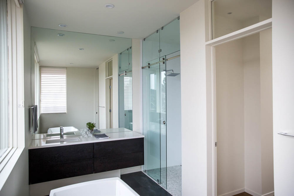 This is an example of a mid-sized modern master bathroom in Calgary with flat-panel cabinets, black cabinets, a freestanding tub, a curbless shower, a one-piece toilet, black tile, ceramic tile, white walls, limestone floors, an undermount sink, engineered quartz benchtops, black floor and a sliding shower screen.
