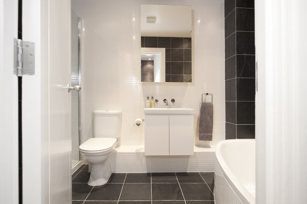 This is an example of a contemporary bathroom in London with a two-piece toilet, white tile and black floor.