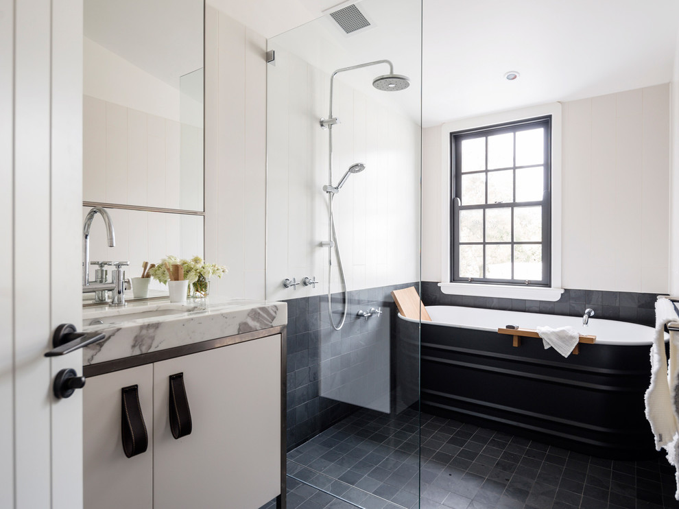 Photo of a contemporary master bathroom in Sydney with an undermount sink, flat-panel cabinets, a freestanding tub, black tile, beige walls, a curbless shower and white cabinets.