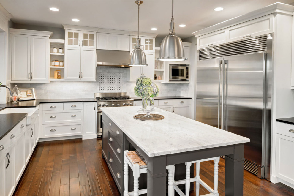 Foto på ett stort funkis vit kök, med en köksö, en rustik diskho, luckor med infälld panel, vita skåp, marmorbänkskiva, grått stänkskydd, stänkskydd i marmor, rostfria vitvaror, mörkt trägolv och brunt golv