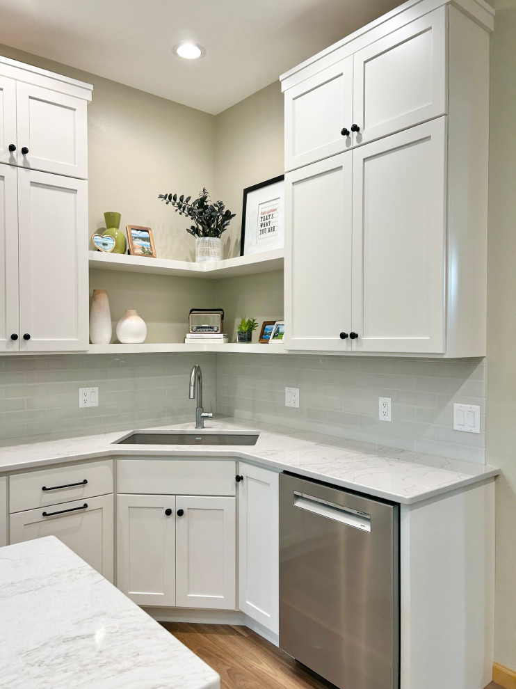 Example of a mid-sized transitional l-shaped medium tone wood floor and brown floor open concept kitchen design with an undermount sink, flat-panel cabinets, white cabinets, quartz countertops, gray backsplash, ceramic backsplash, stainless steel appliances, an island and white countertops