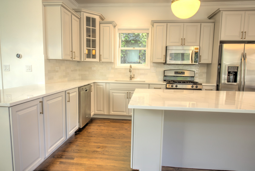 Mid-sized contemporary l-shaped eat-in kitchen in Chicago with an undermount sink, recessed-panel cabinets, white cabinets, quartz benchtops, white splashback, ceramic splashback, stainless steel appliances, dark hardwood floors, with island, brown floor and white benchtop.