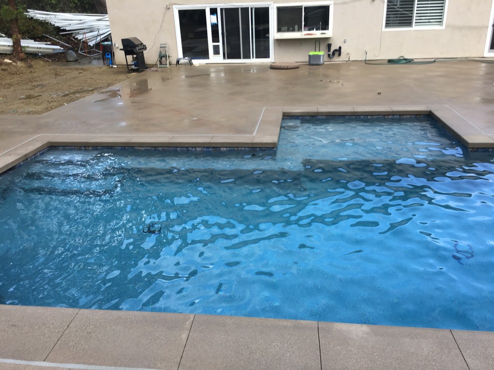 This is an example of a mid-sized tropical backyard custom-shaped lap pool in Orange County with a hot tub and concrete slab.