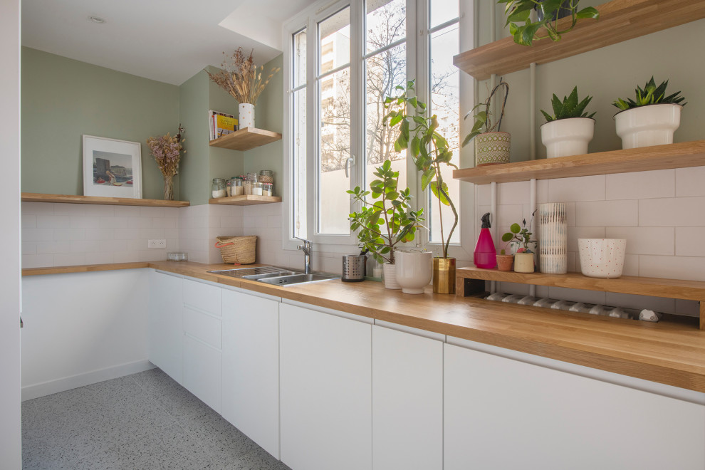 Foto på ett mellanstort beige kök, med en dubbel diskho, släta luckor, vita skåp, träbänkskiva, vitt stänkskydd, stänkskydd i porslinskakel, integrerade vitvaror, terrazzogolv och vitt golv