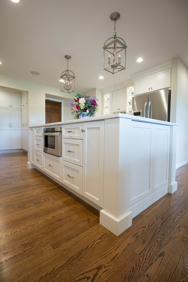 Huge transitional medium tone wood floor open concept kitchen photo with an undermount sink, shaker cabinets, white cabinets, marble countertops, white backsplash, ceramic backsplash, stainless steel appliances and two islands