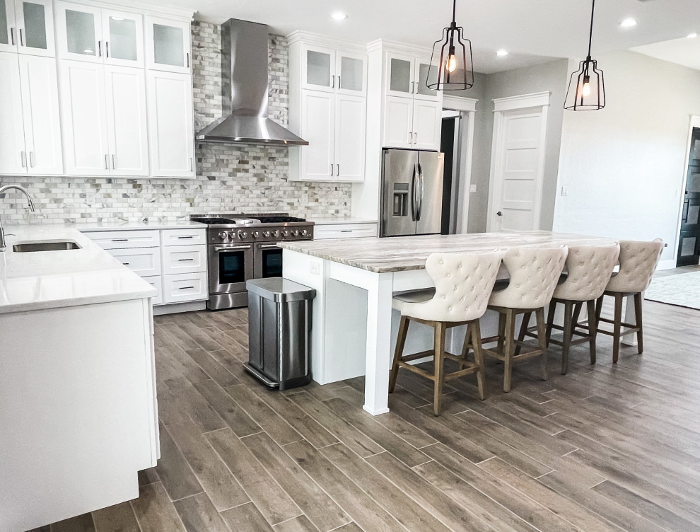 Large transitional l-shaped medium tone wood floor and brown floor eat-in kitchen photo with an undermount sink, beaded inset cabinets, white cabinets, marble countertops, multicolored backsplash, ceramic backsplash, stainless steel appliances, an island and multicolored countertops