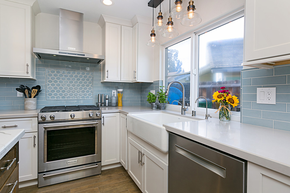 Photo of an expansive beach style l-shaped eat-in kitchen in San Diego with a farmhouse sink, recessed-panel cabinets, white cabinets, granite benchtops, blue splashback, subway tile splashback, stainless steel appliances, porcelain floors, with island and brown floor.