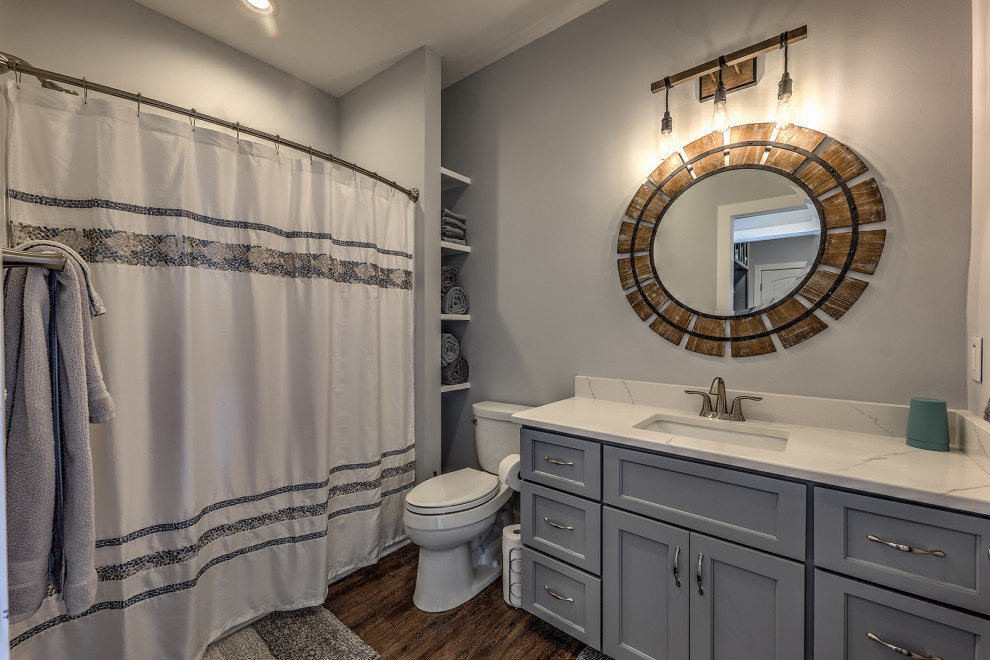Exempel på ett mellanstort amerikanskt vit vitt badrum, med skåp i shakerstil, grå skåp, ett badkar i en alkov, en dusch/badkar-kombination, en toalettstol med separat cisternkåpa, grå väggar, vinylgolv, ett undermonterad handfat, bänkskiva i kvarts, brunt golv och dusch med duschdraperi