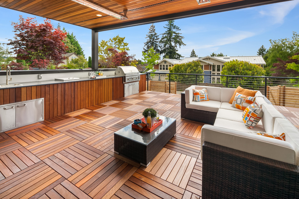 Expansive midcentury deck in Seattle with a roof extension, metal railing and an outdoor kitchen.