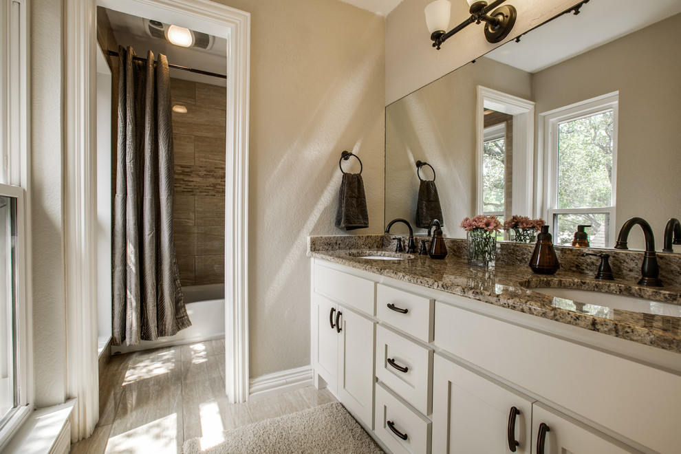 Inspiration for a mid-sized transitional bathroom in Dallas with shaker cabinets, white cabinets, an alcove tub, an alcove shower, a one-piece toilet, gray tile, travertine, grey walls, ceramic floors, an undermount sink, granite benchtops, beige floor and a shower curtain.