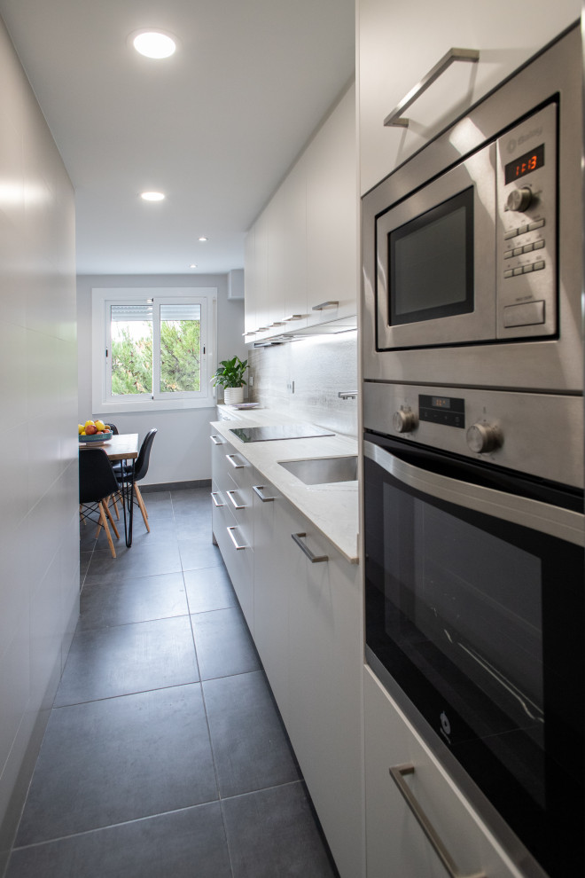 This is an example of a mid-sized contemporary single-wall open plan kitchen in Barcelona with a single-bowl sink, recessed-panel cabinets, white cabinets, marble benchtops, brown splashback, ceramic splashback, stainless steel appliances, ceramic floors, no island, grey floor and beige benchtop.