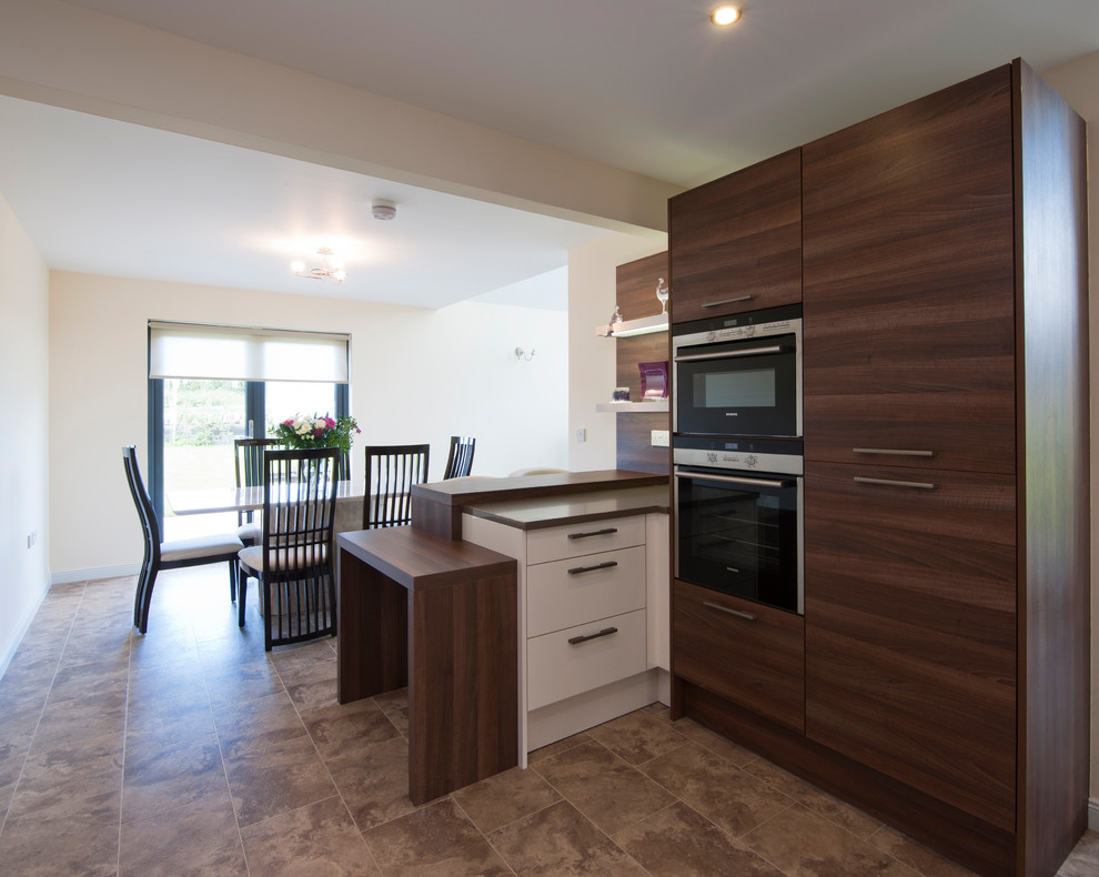 This is an example of a large modern l-shaped open plan kitchen in Other with a double-bowl sink, flat-panel cabinets, dark wood cabinets, granite benchtops, glass sheet splashback, stainless steel appliances, ceramic floors, a peninsula, beige floor and grey benchtop.