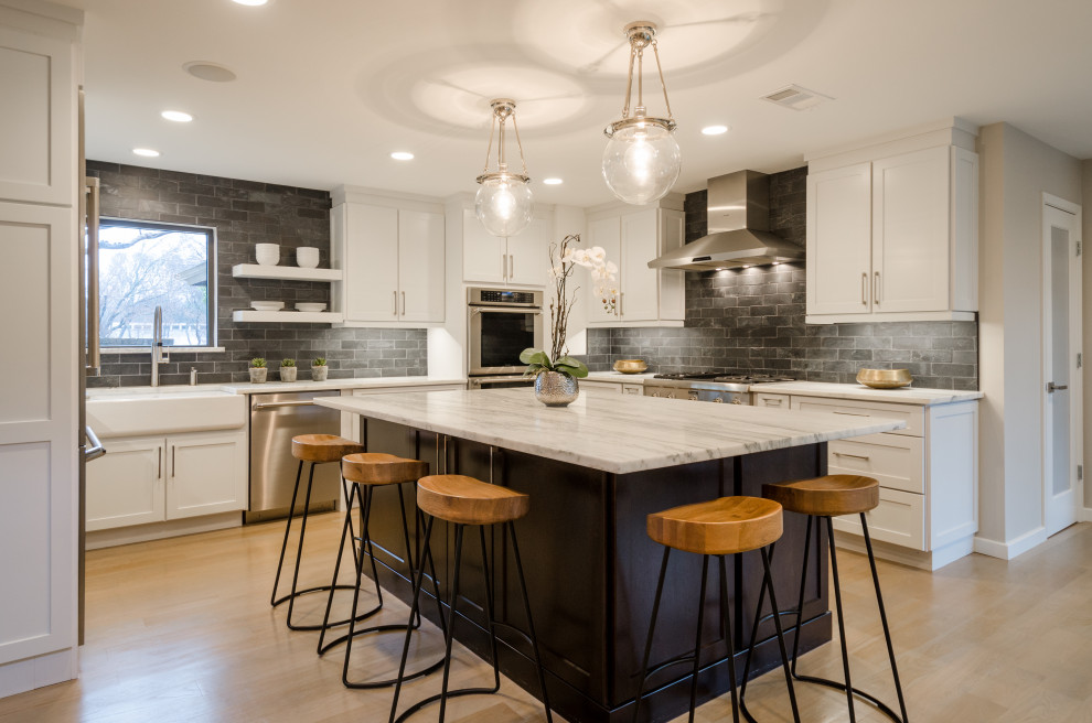 This is an example of a large country u-shaped eat-in kitchen in Portland with a farmhouse sink, shaker cabinets, white cabinets, marble benchtops, black splashback, marble splashback, stainless steel appliances, light hardwood floors, with island, beige floor and white benchtop.