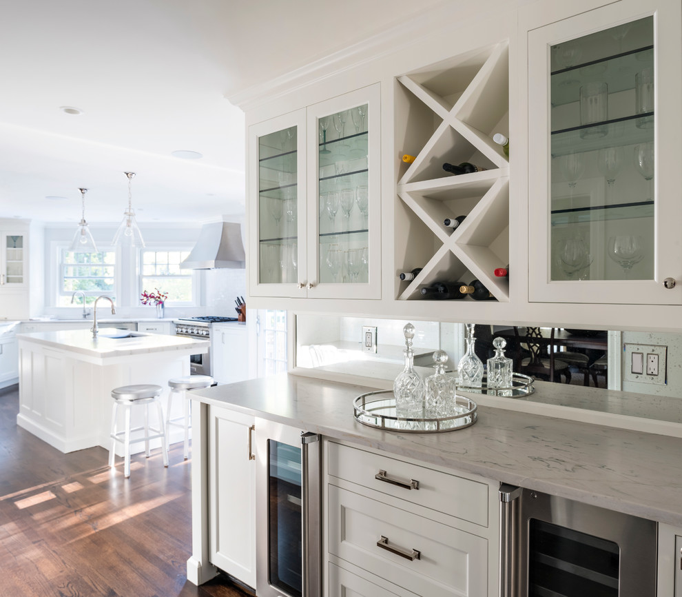 Mid-sized transitional l-shaped eat-in kitchen in New York with an undermount sink, shaker cabinets, white cabinets, quartzite benchtops, white splashback, ceramic splashback, stainless steel appliances, dark hardwood floors and with island.