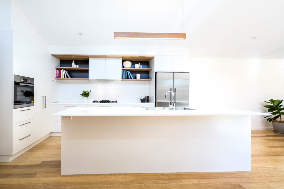 Design ideas for a mid-sized contemporary galley open plan kitchen in Canberra - Queanbeyan with a drop-in sink, white cabinets, quartz benchtops, white splashback, subway tile splashback, stainless steel appliances, light hardwood floors, with island, beige floor and white benchtop.