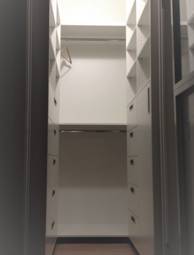 Diseño de armario vestidor unisex contemporáneo pequeño con armarios con paneles lisos, puertas de armario blancas, suelo laminado, suelo marrón y papel pintado