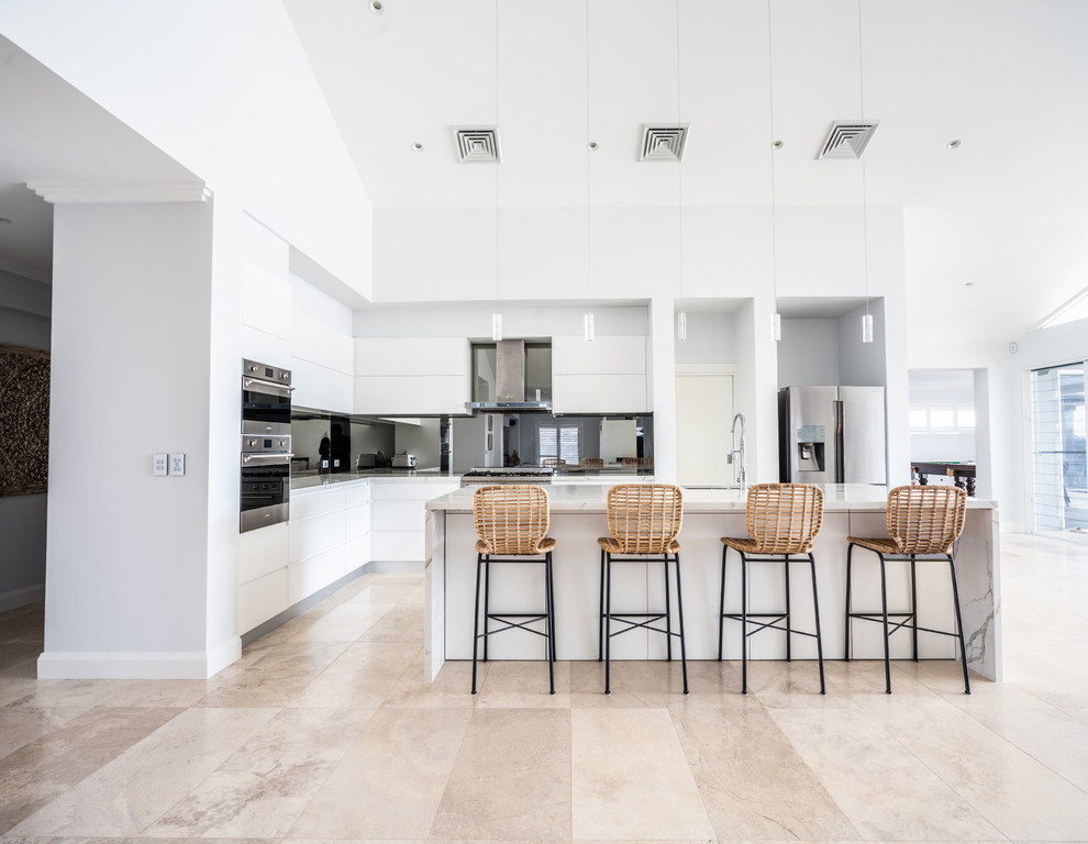 This is an example of a mid-sized contemporary l-shaped open plan kitchen in Sydney with flat-panel cabinets, white cabinets, mirror splashback, white benchtop, an undermount sink, quartz benchtops, metallic splashback, stainless steel appliances, with island and beige floor.