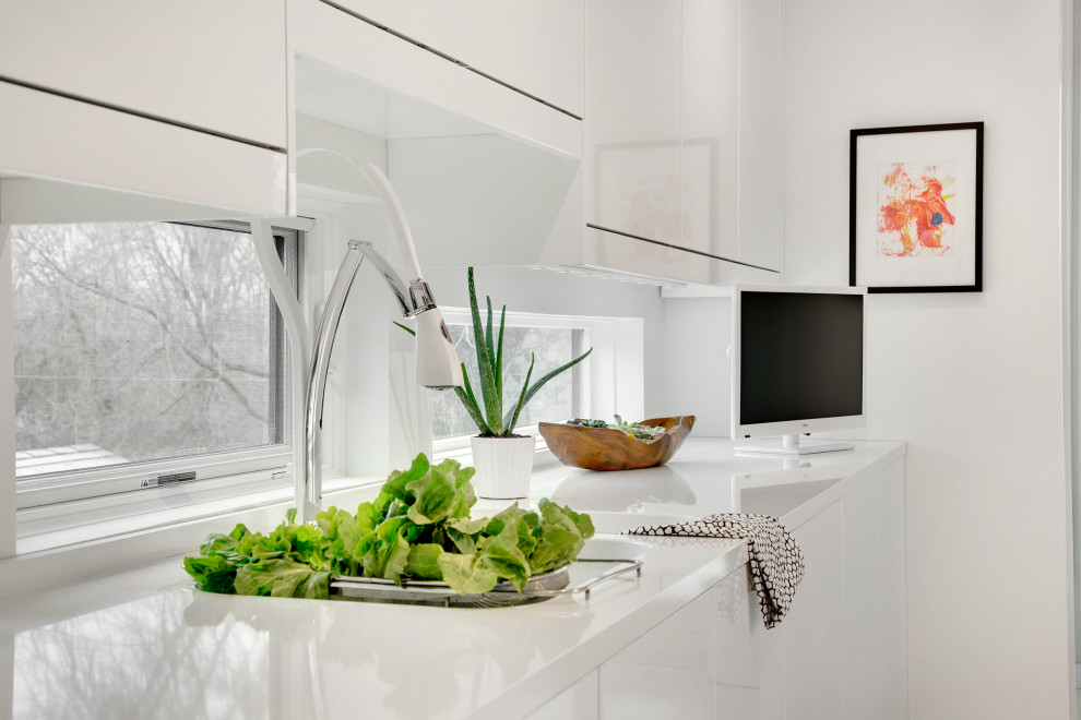 Example of a mid-sized minimalist galley light wood floor and white floor home design design with an undermount sink, flat-panel cabinets, white cabinets, quartz countertops, window backsplash, white appliances and an island