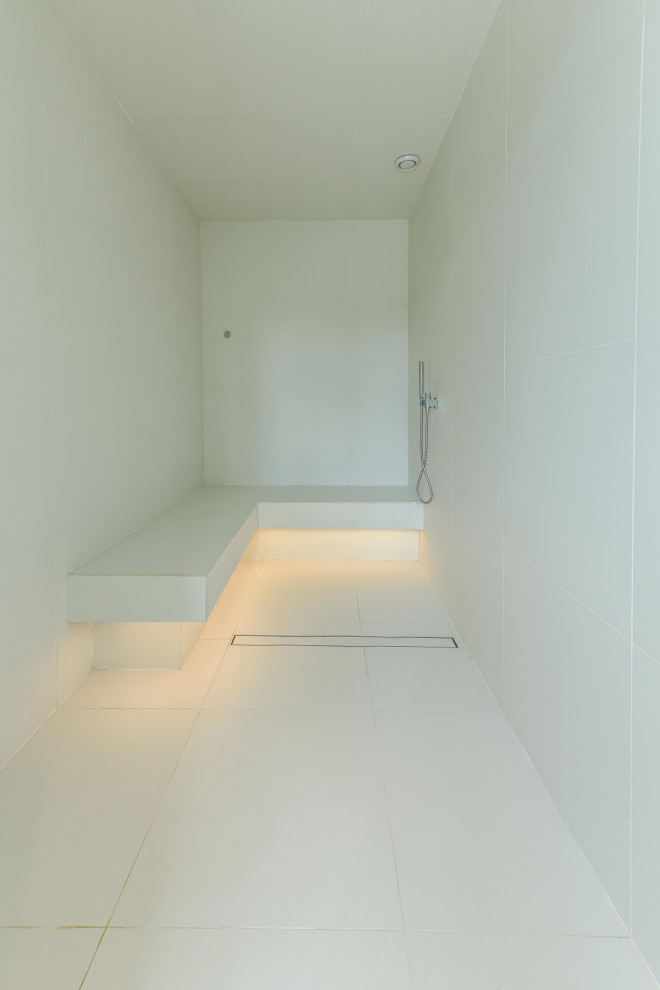 Cette image montre une très grande salle de bain design avec un espace douche bain, un carrelage blanc, des carreaux de céramique, un mur blanc, un sol blanc, une cabine de douche à porte battante et un banc de douche.