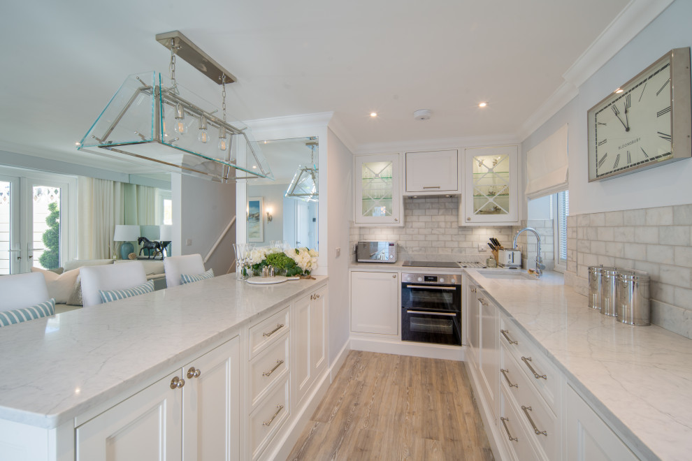 Design ideas for a mid-sized beach style u-shaped eat-in kitchen in Other with an undermount sink, shaker cabinets, white cabinets, quartzite benchtops, white splashback, marble splashback, black appliances, a peninsula, grey floor and white benchtop.