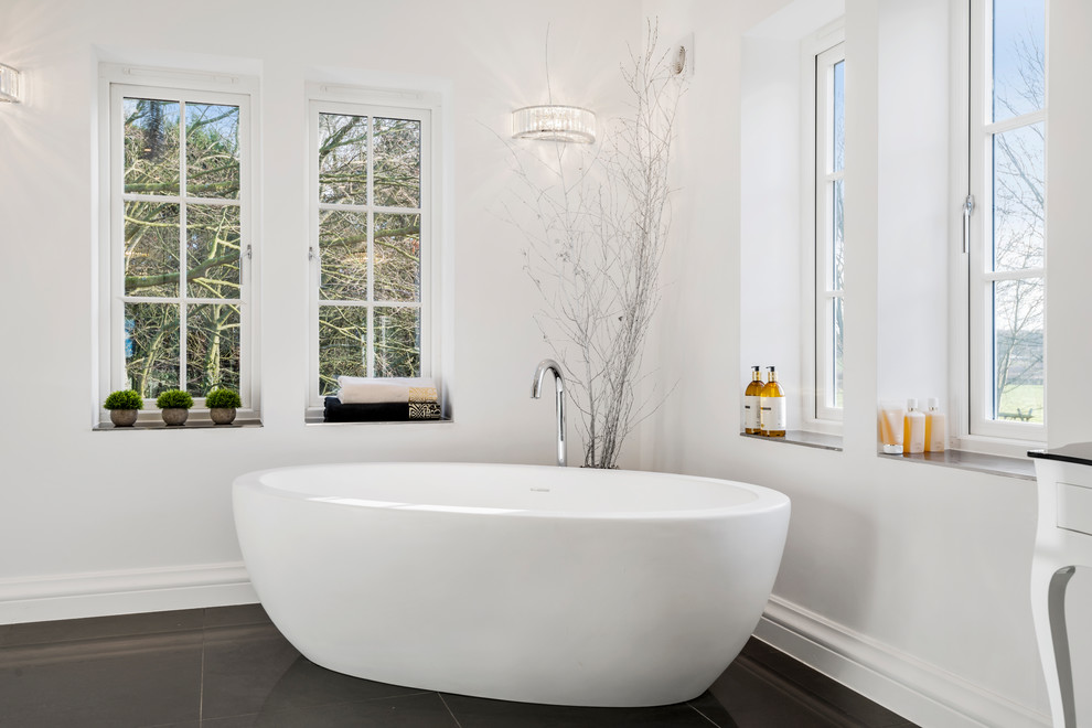 Design ideas for a large contemporary master bathroom in West Midlands with furniture-like cabinets, white cabinets, a freestanding tub, white tile, porcelain floors, a console sink, glass benchtops and black floor.