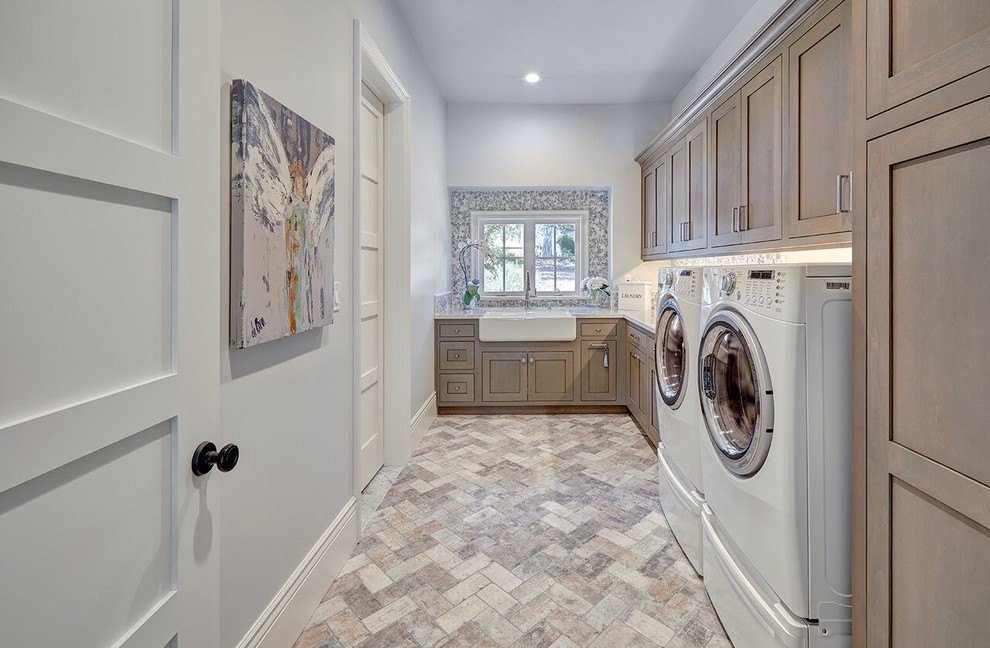 Design ideas for a large traditional l-shaped dedicated laundry room in Sacramento with a farmhouse sink, shaker cabinets, dark wood cabinets, grey walls, travertine floors, a side-by-side washer and dryer and multi-coloured floor.