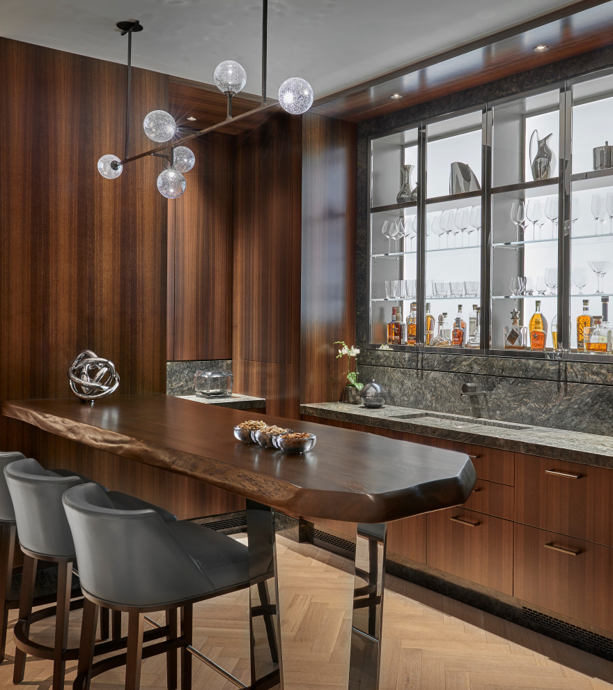 Photo of a contemporary seated home bar in Chicago with an integrated sink, open cabinets, grey splashback, light hardwood floors and grey benchtop.