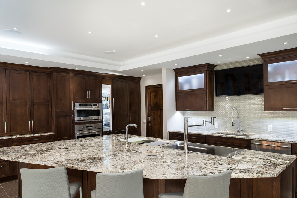 Large transitional ceramic tile and beige floor eat-in kitchen photo with an undermount sink, shaker cabinets, brown cabinets, granite countertops, white backsplash, glass tile backsplash, stainless steel appliances and an island
