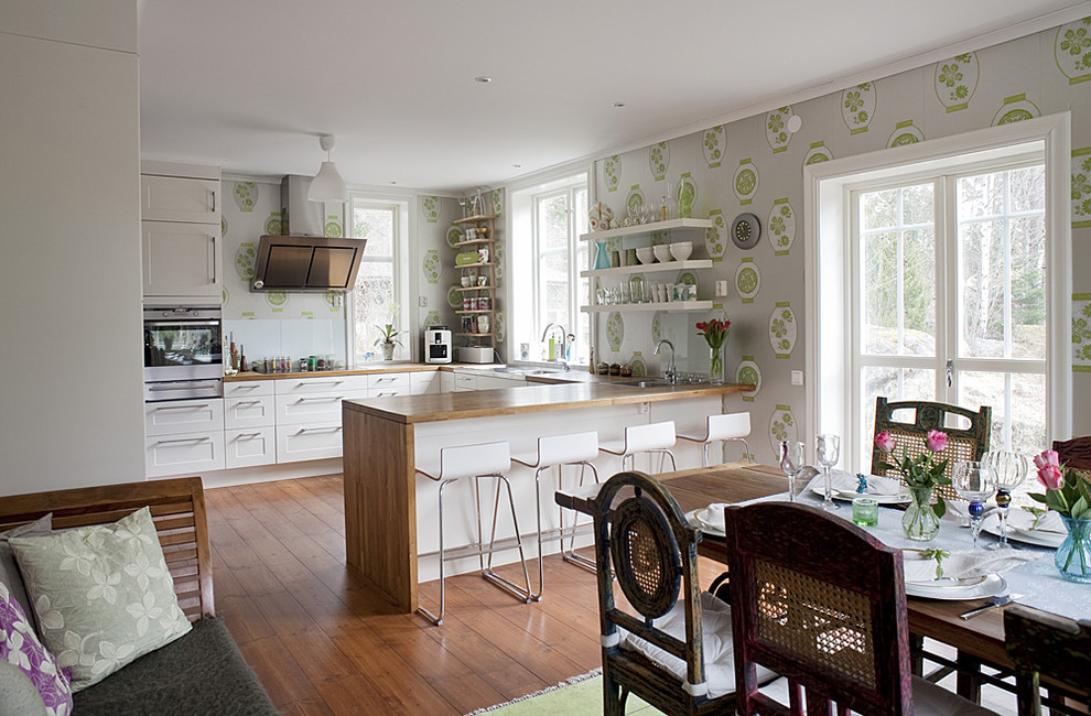 This is an example of a mid-sized eclectic u-shaped eat-in kitchen in Stockholm with wood benchtops, white cabinets, stainless steel appliances, medium hardwood floors, no island and recessed-panel cabinets.