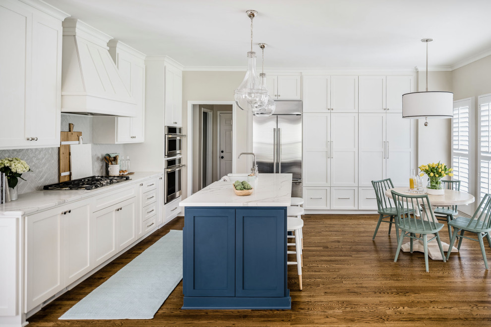 Inspiration for a medium sized classic l-shaped kitchen/diner in Charlotte with a belfast sink, shaker cabinets, white cabinets, engineered stone countertops, grey splashback, porcelain splashback, stainless steel appliances, medium hardwood flooring, an island, brown floors and white worktops.