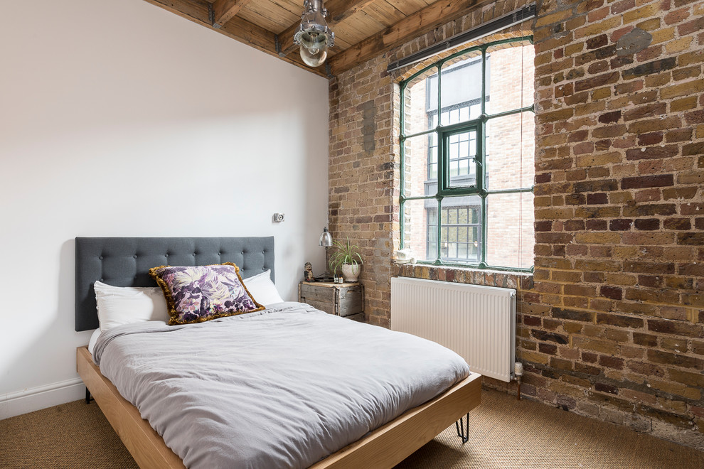 This is an example of a mid-sized industrial guest bedroom in London with carpet, beige floor and white walls.
