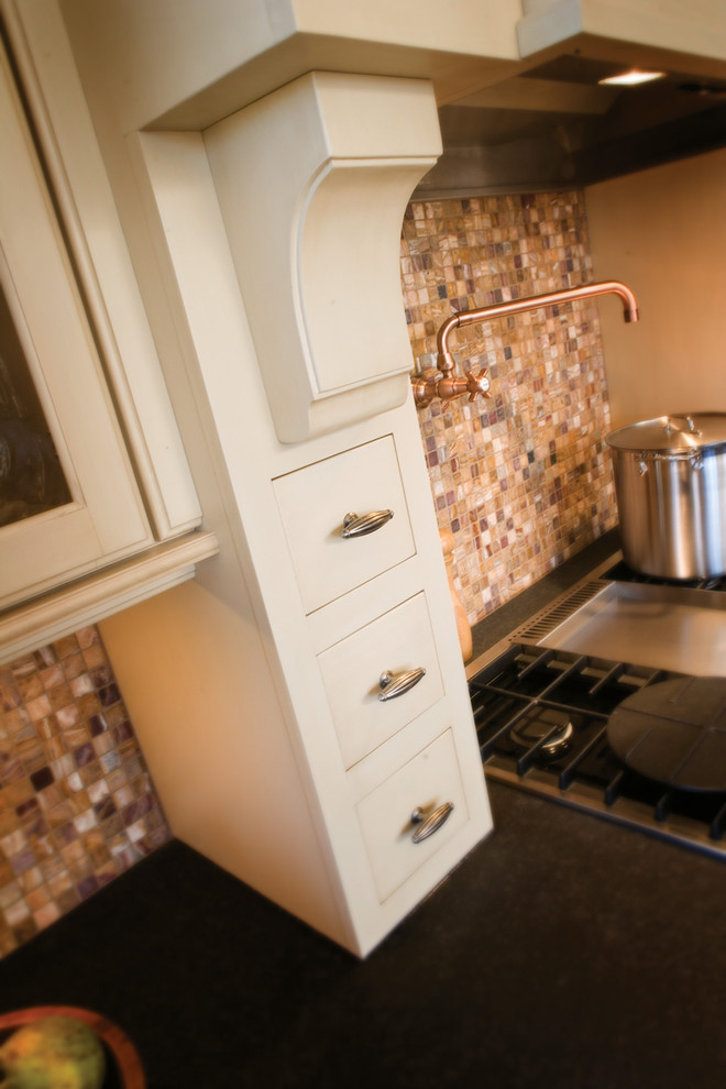 Traditional kitchen in Minneapolis with a farmhouse sink, raised-panel cabinets, white cabinets, metallic splashback, glass tile splashback, stainless steel appliances, porcelain floors and with island.