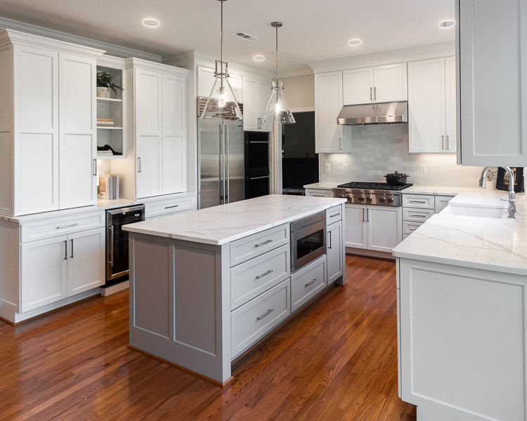 Large transitional u-shaped eat-in kitchen in DC Metro with a farmhouse sink, shaker cabinets, white cabinets, quartz benchtops, white splashback, subway tile splashback, stainless steel appliances, medium hardwood floors, with island, red floor and white benchtop.