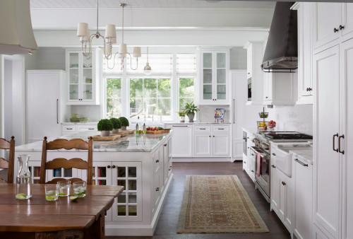 Bright farmhouse-style kitchen with white kitchen cabinets, marble island, farmhouse sink, and large windows bringing in natural light.