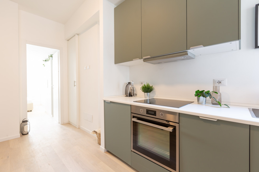 Photo of a small modern single-wall open plan kitchen in Milan with a single-bowl sink, flat-panel cabinets, green cabinets, laminate countertops, white splashback, stainless steel appliances, medium hardwood flooring, no island and white worktops.