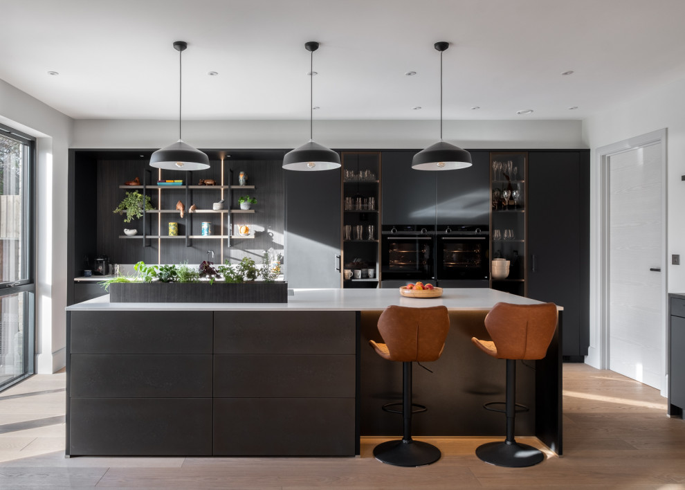 Photo of a large contemporary eat-in kitchen in Gloucestershire with a drop-in sink, flat-panel cabinets, black cabinets, solid surface benchtops, white splashback, black appliances, with island and white benchtop.